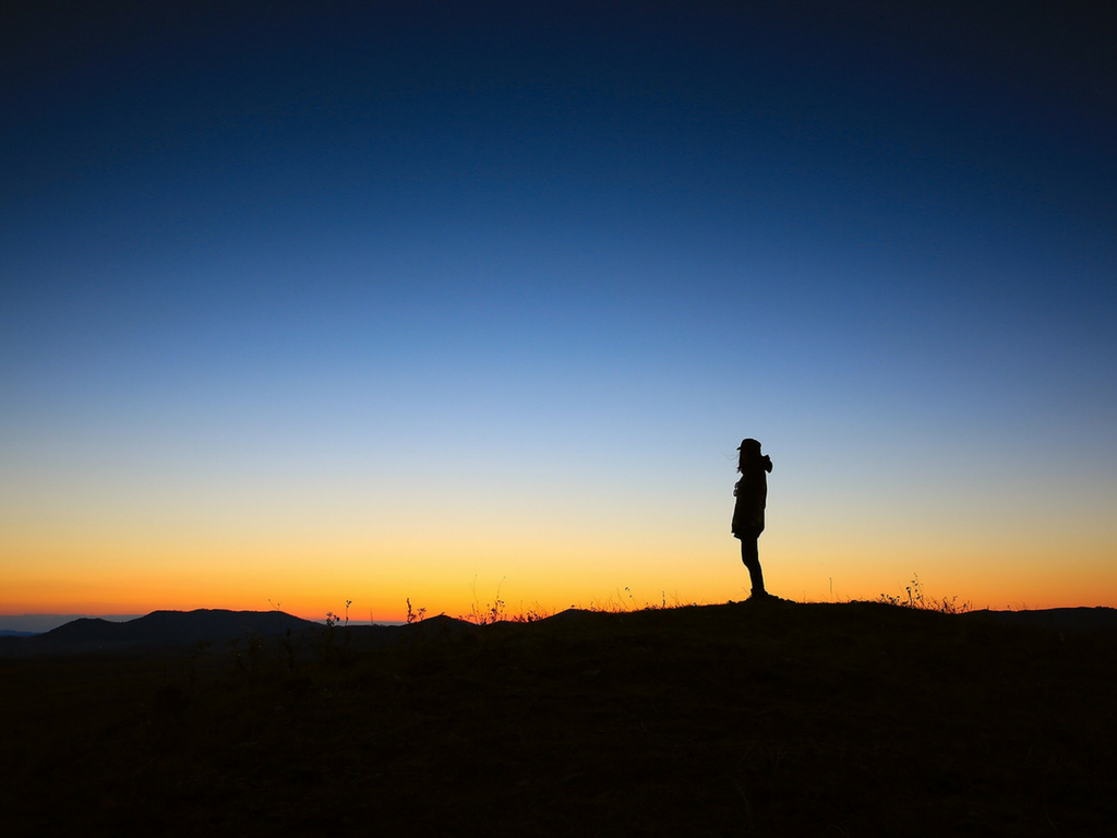 A lone silhouetted person stands against a sunset.