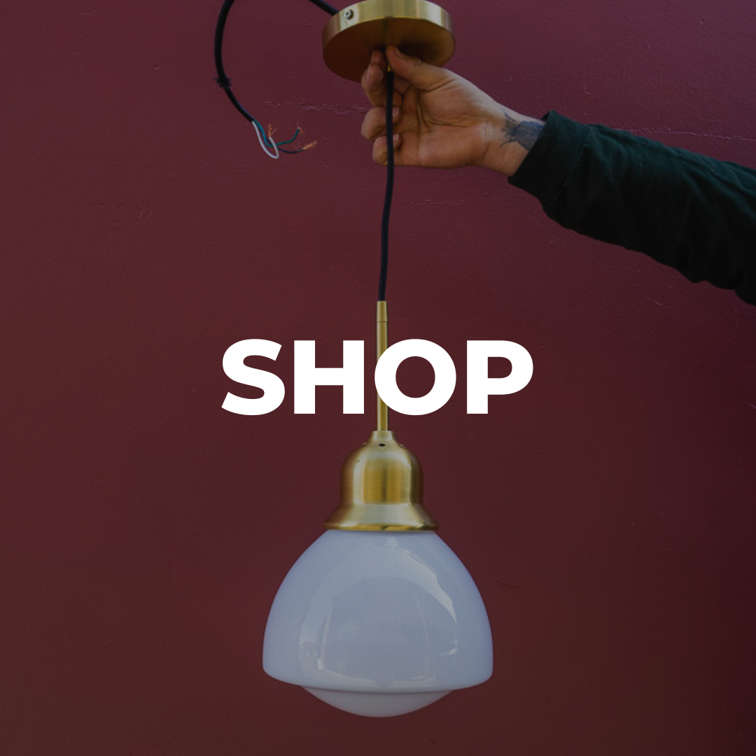 SHOP. Background: Hanging pendant light with a maroon background being held by a tattooed hand.