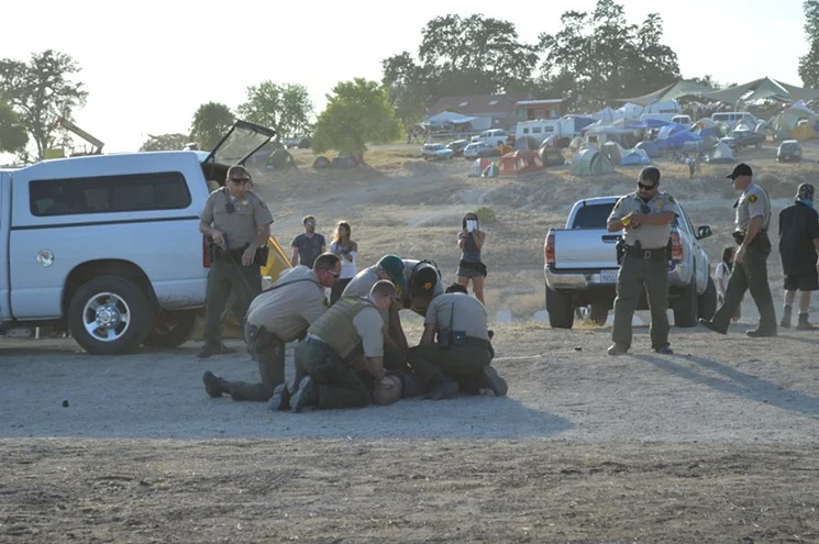 Image of a woman getting tazed by police officers at Lightning in a Bottle 2014 📷: LA Weekly