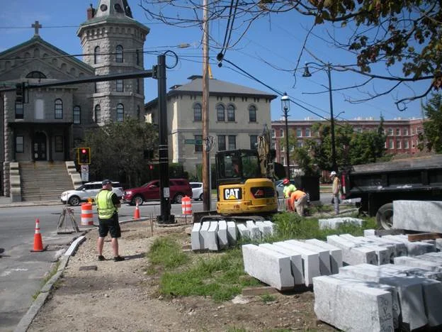 Construction crews install new curbs with a new streetlamp in background.