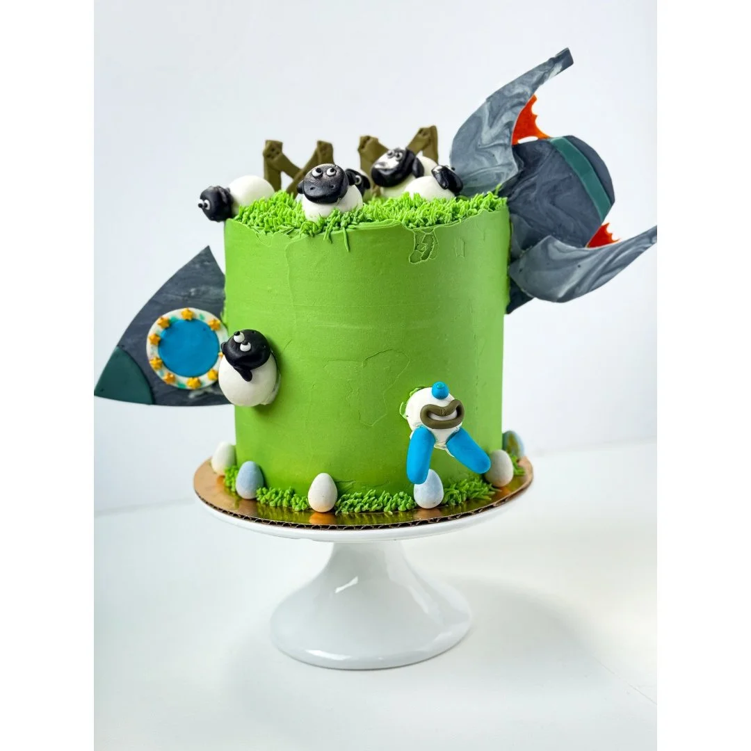 Cake #12 of 2025: Chocolate cake with chocolate frosting designed by my son. This cake includes a spaceship crashing into a field with sheep. There is also a one-eyed alien climbing out of the spaceship. All I can say is that this kid comes up with s