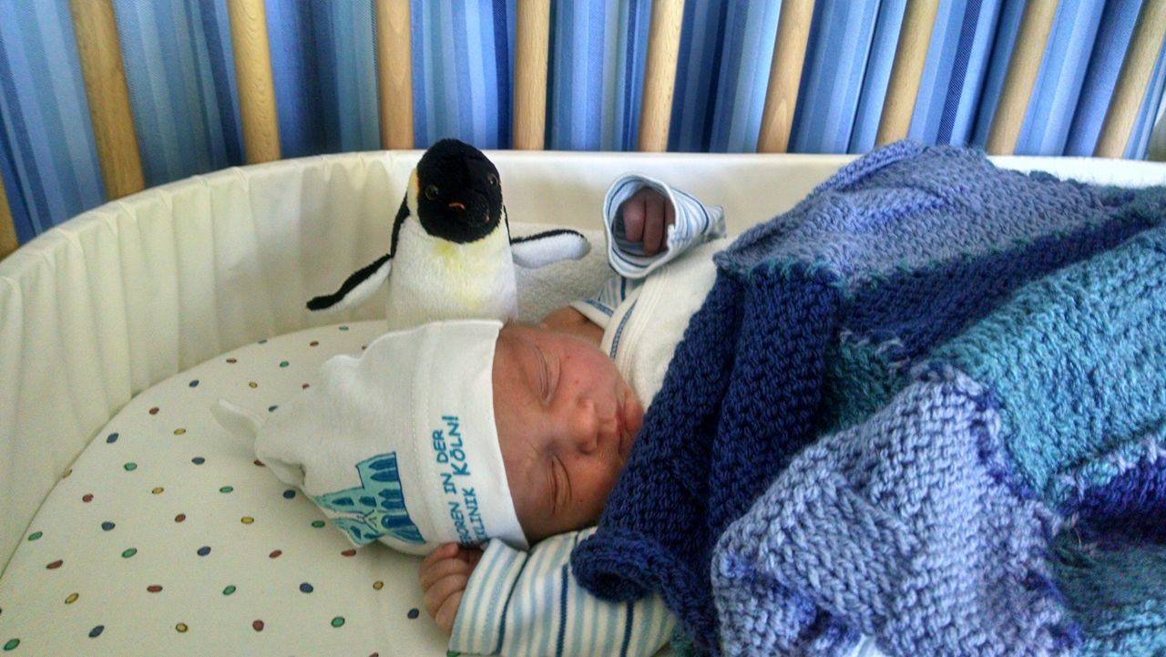 Throwing his arms up from under the blanket I knit him. Can we please take a moment to appreciate the color coordination between his onesie, the curtain behind the BabyBay, the blanket, and the Uniklinik hat?