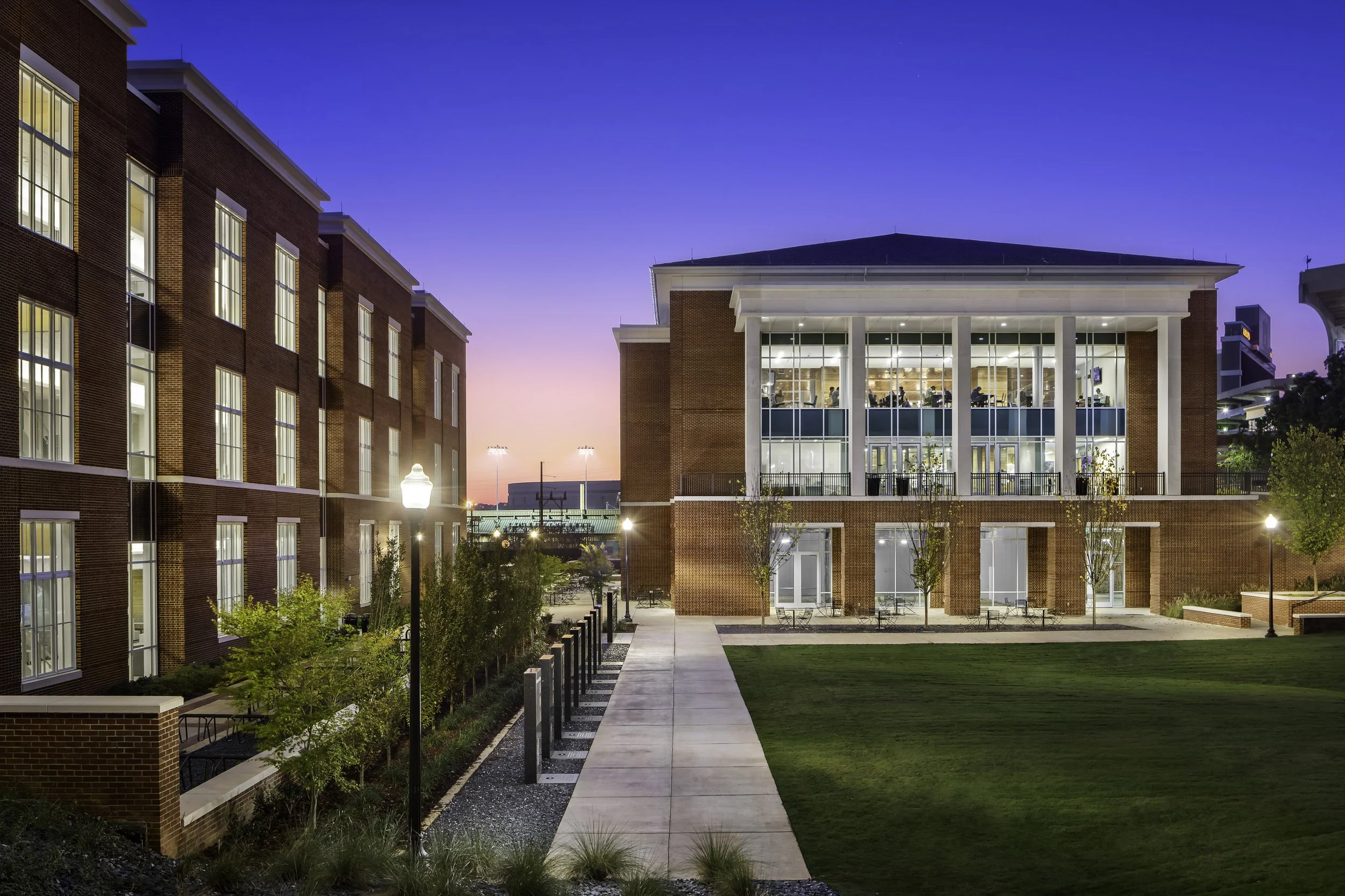 Modern university building with large windows, brick exterior, and landscaped courtyard at dusk.