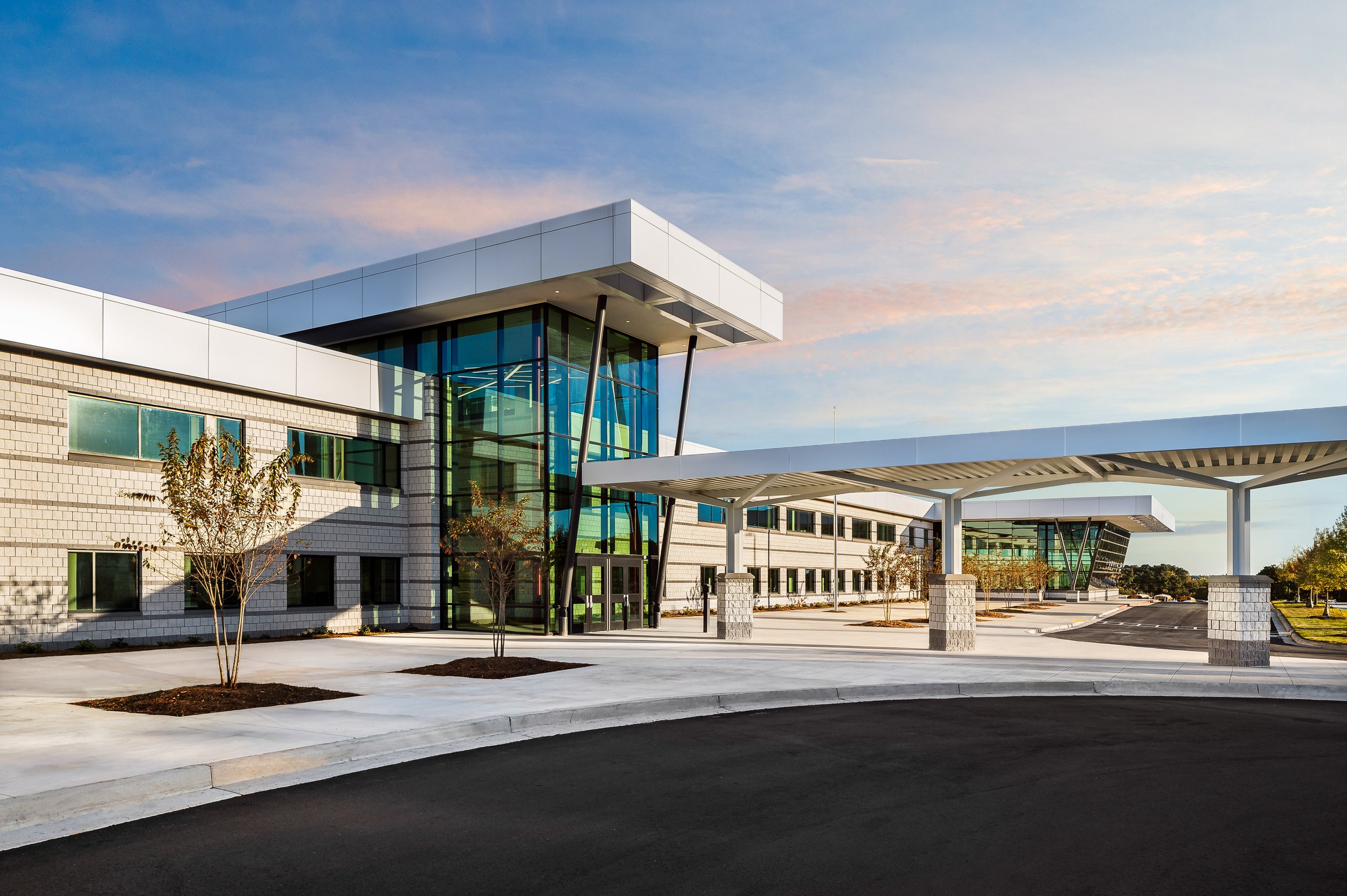 Modern educational building with glass and brick facade, covered entrance area, trees, and clear sky.