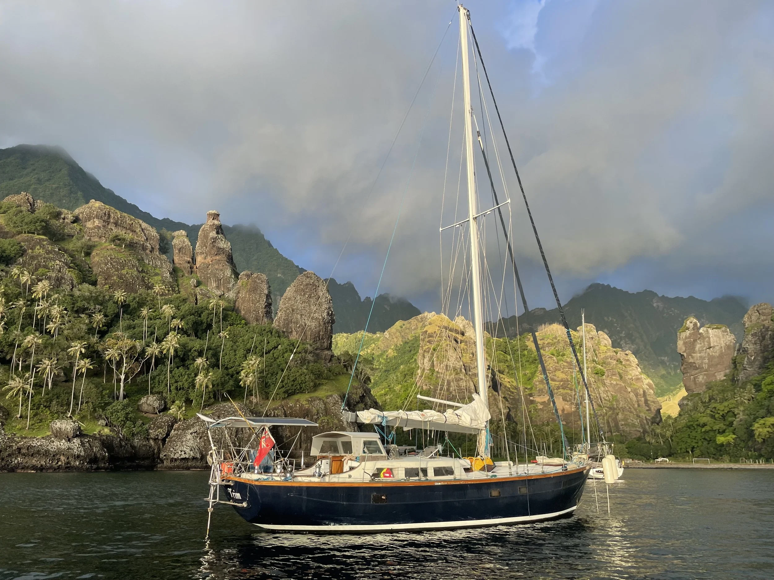 Sailboat anchored in a bay with lush green mountains and rocky cliffs in the background.
