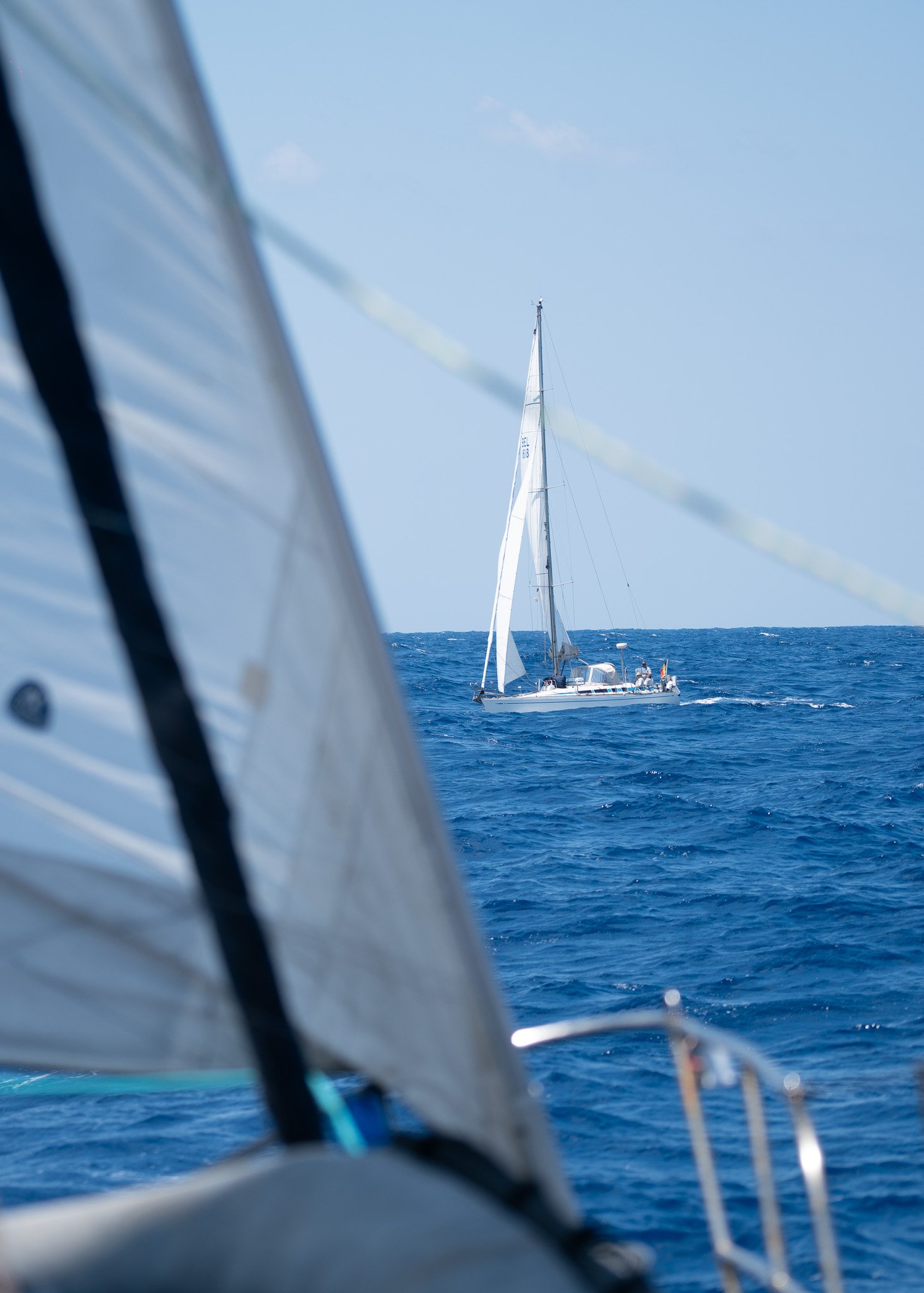 View of sailing boats on the ocean, one in the distance and part of another in the foreground.