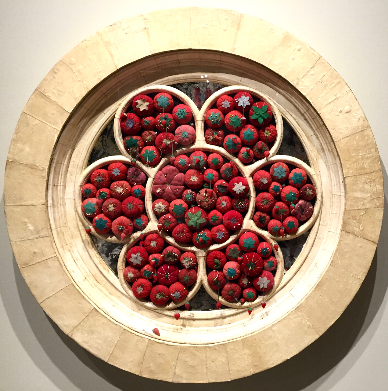 This piece, made of tomato shaped pincushions, wood, plaster, and mirrors is called " Rose Window ," and it is part of Marianne Lettieri's exhibit, "Reflections." It is on display at the Museum of Craft and Design in San Francisco through January 22, 2017.
