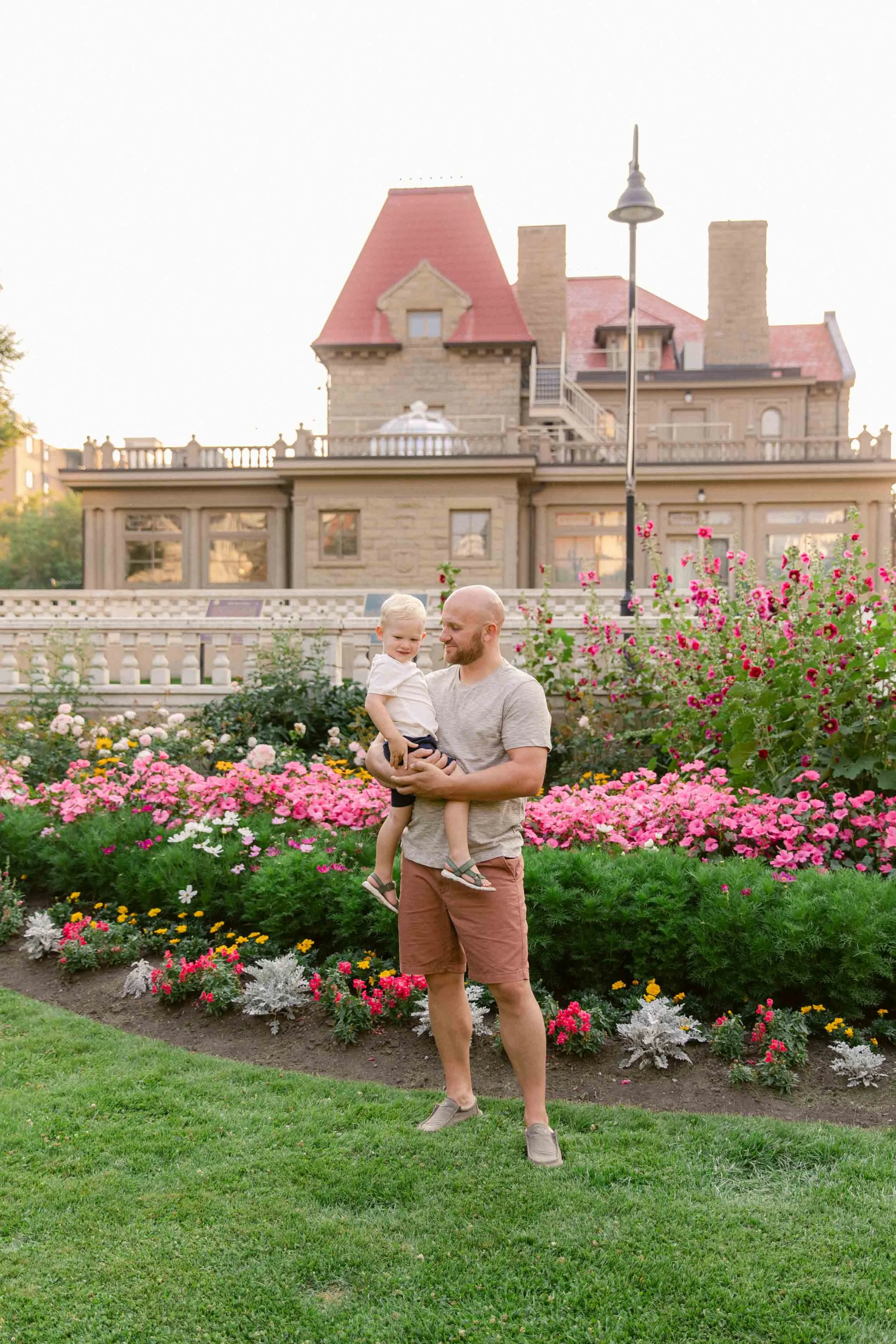 A family photo shoot at the Beaulieu Gardens at Lougheed House, Father holding son in front of pink garden