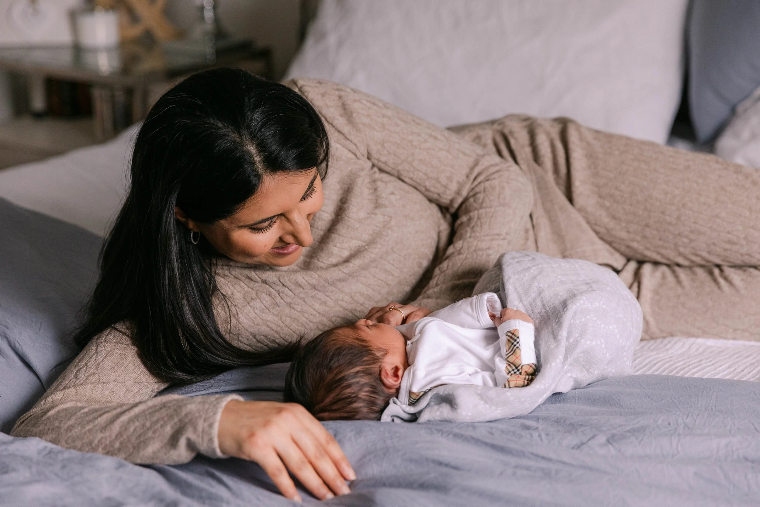 Mother and baby laying on bed together, newborn lifestyle shoot, wearing cream, white and black neutrals, indian mother and son