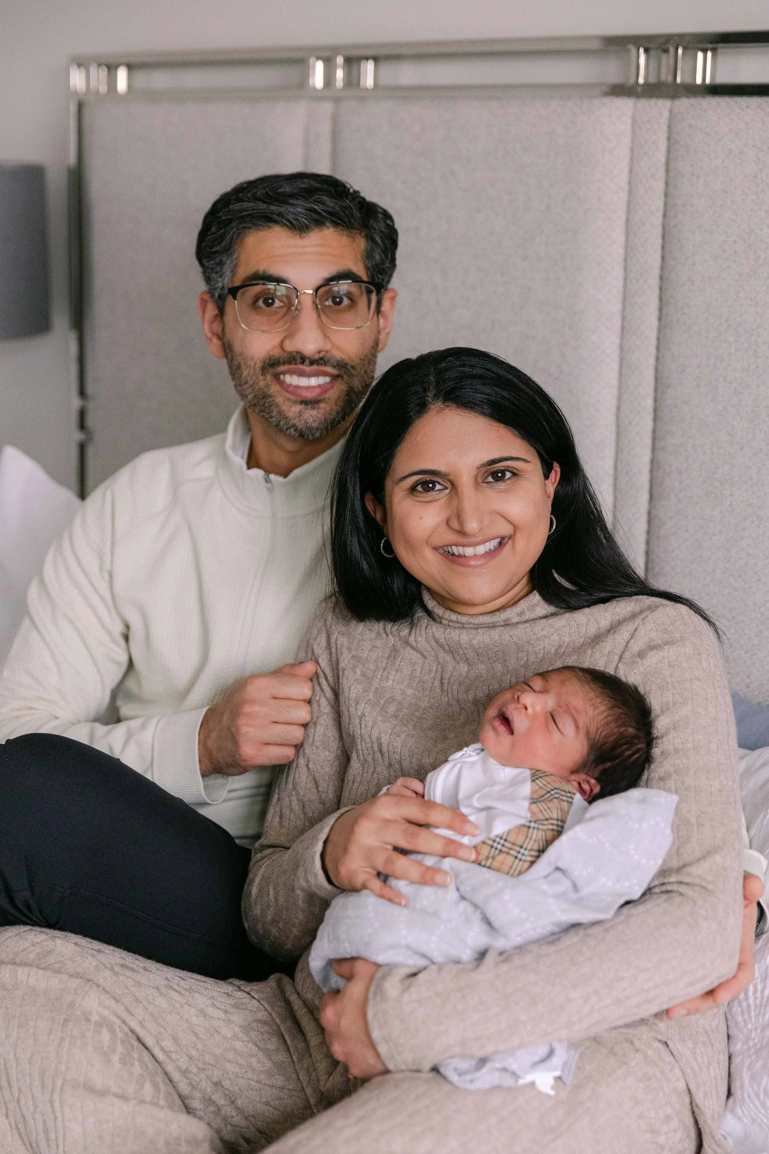 mom, dad and baby on bed, newborn lifestyle shoot, wearing cream, white and black neutrals, indian mother, father and son