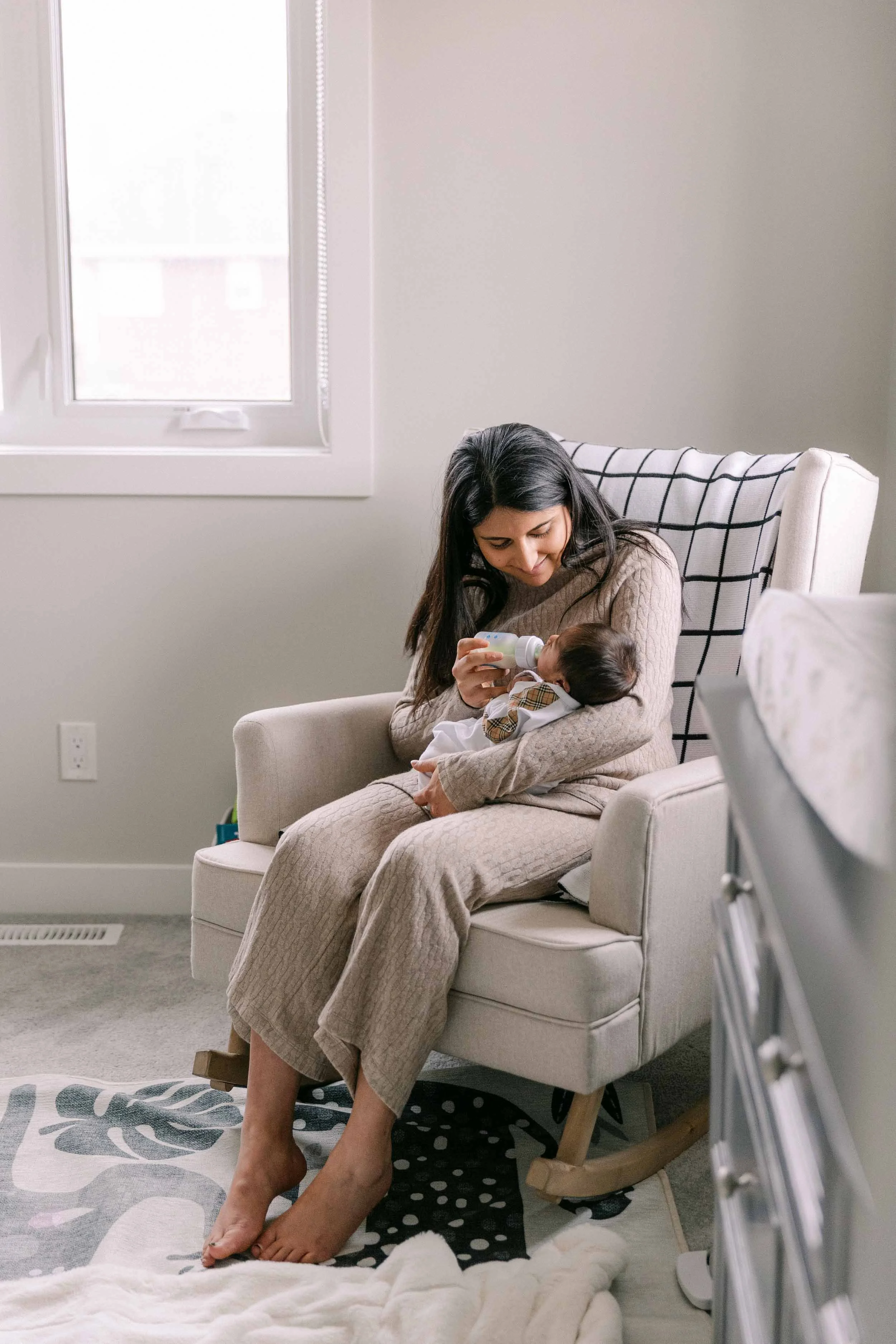 mom and baby in upholstered rocking chair, newborn lifestyle shoot, wearing cream, white and black neutrals, indian mother and son