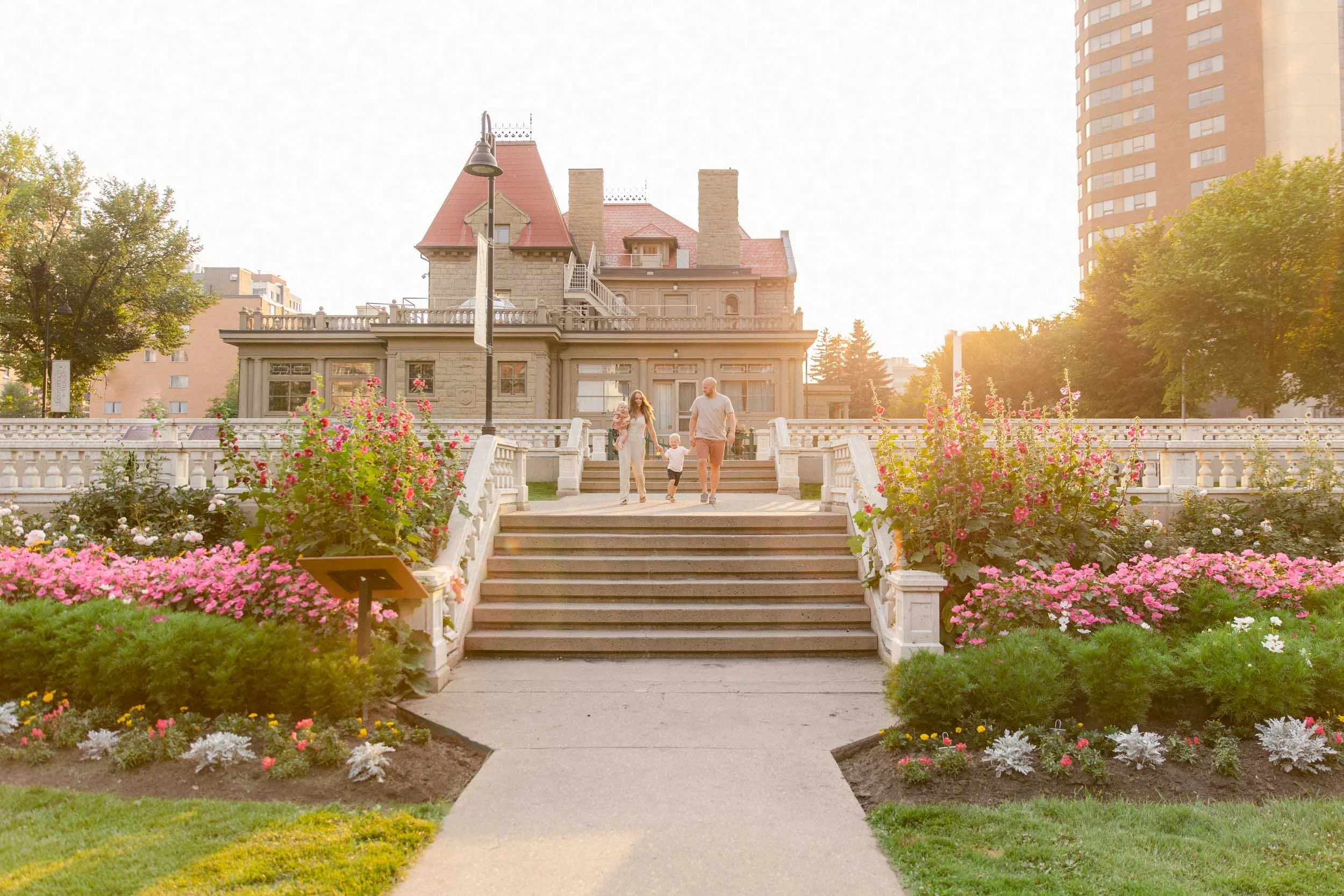 A family photo shoot at the Beaulieu Gardens at Lougheed House, walking along the terrace as they swing their child back and forth, dressed in dusty rose, creams and miniature floral patterns