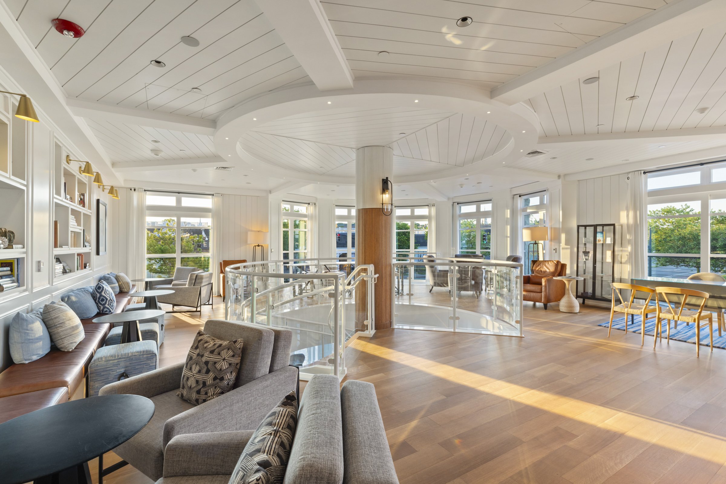 Bright, spacious living room with white walls, wood flooring, large windows, comfortable chairs, sofas, and decorative lamps.
