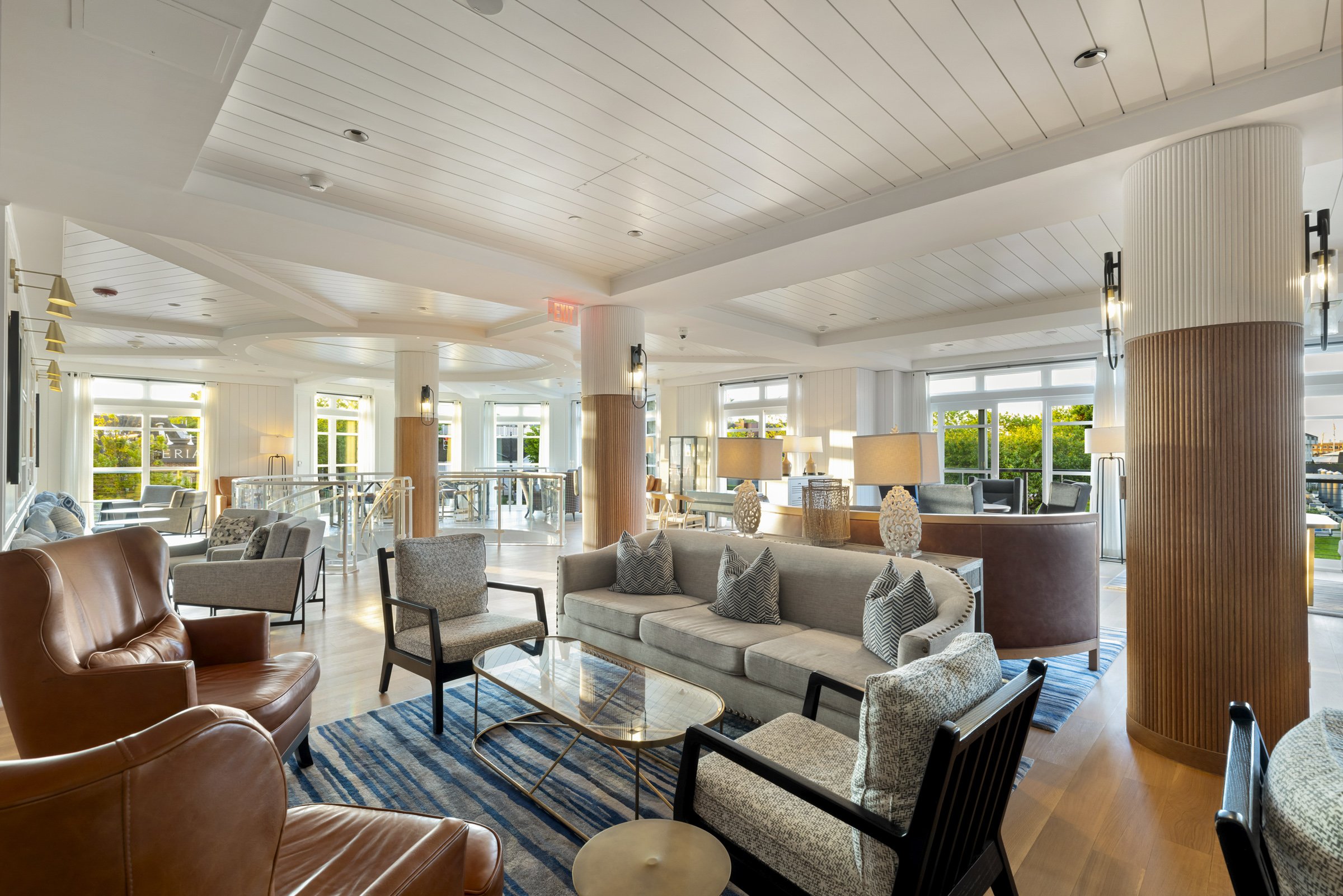 Elegant hotel lobby with various armchairs, sofas, tables, and large windows with greenery outside.