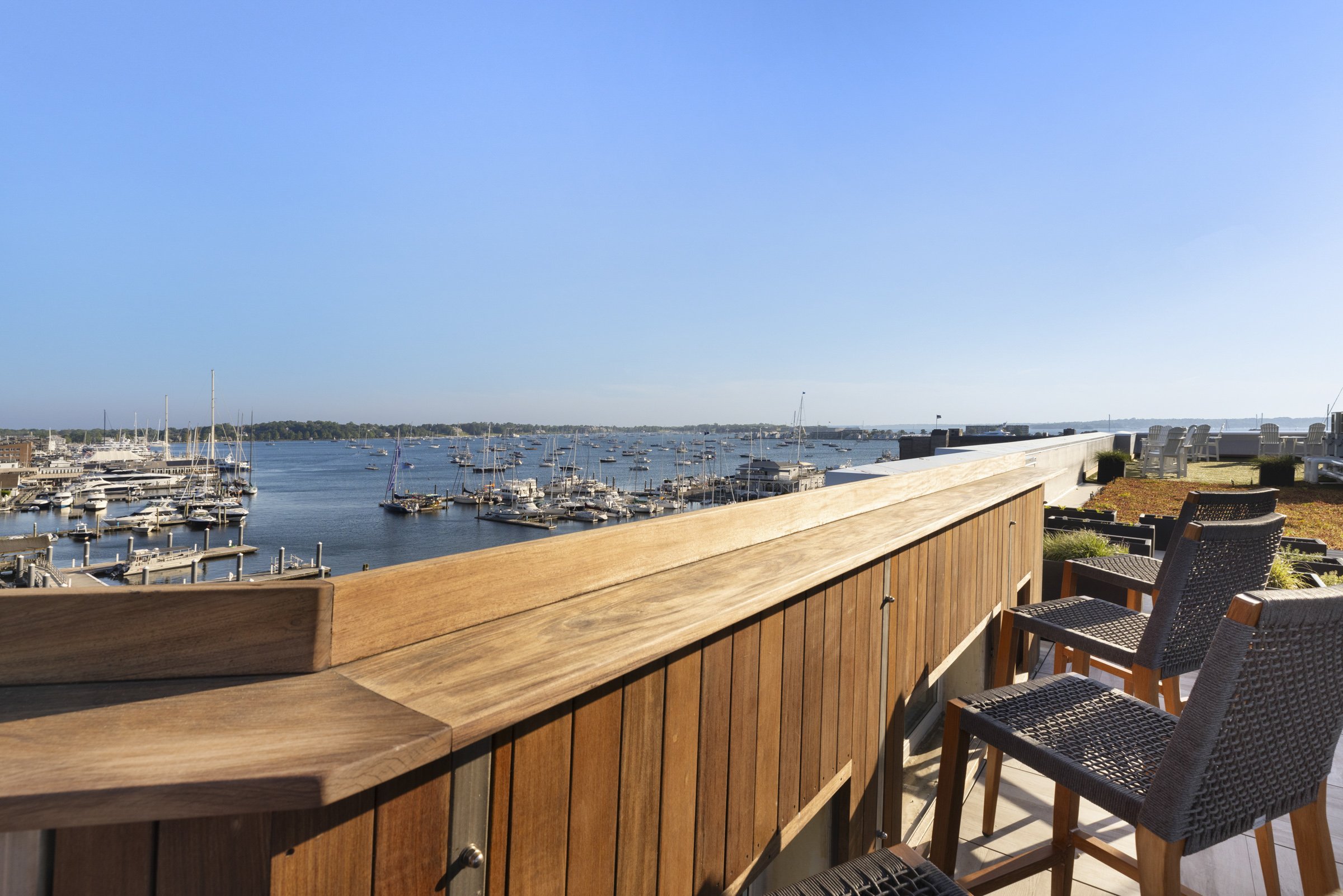 View from a wooden balcony overlooking a marina filled with boats on a bright, clear day with blue sky.