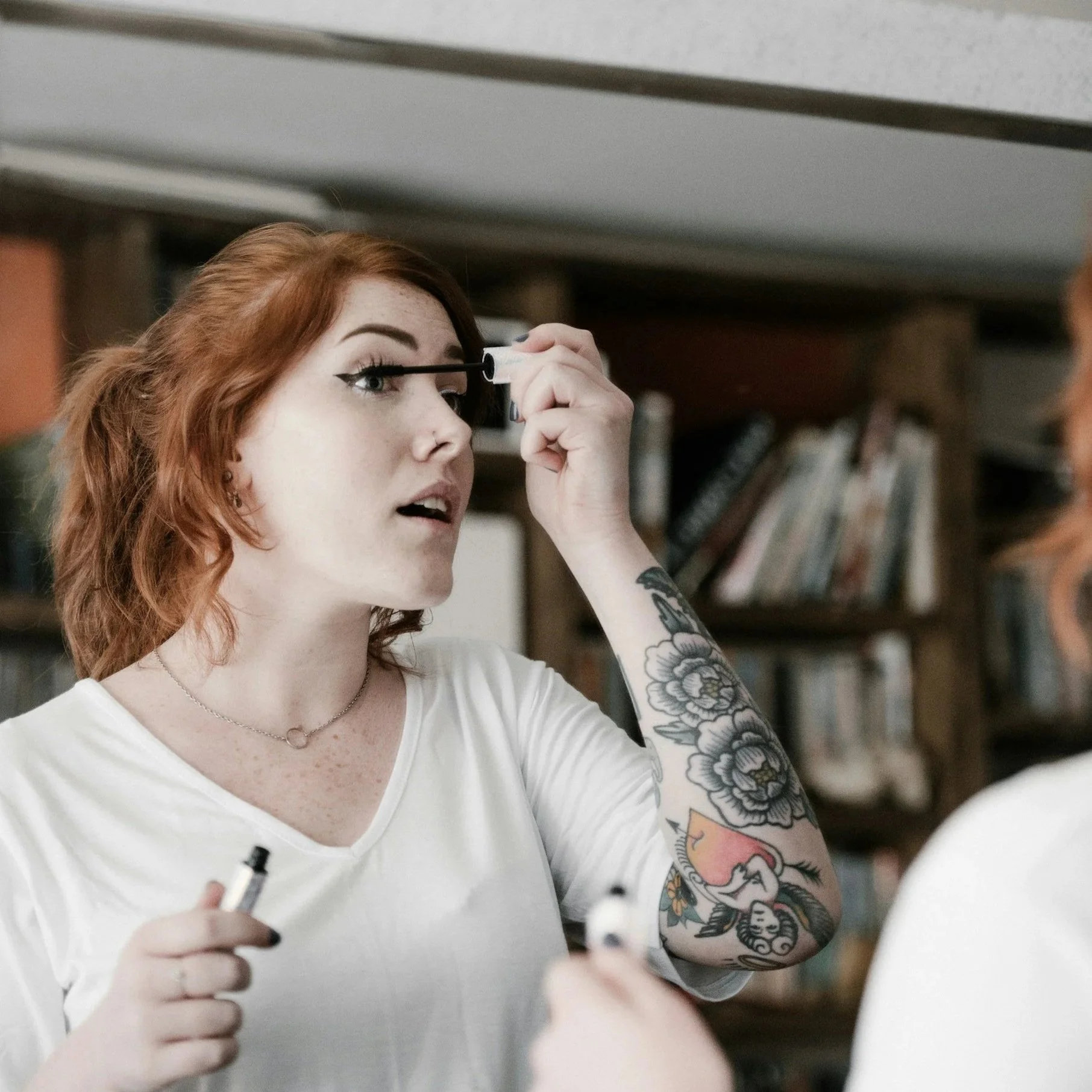 Red-haired woman applying mascara while looking in a mirror