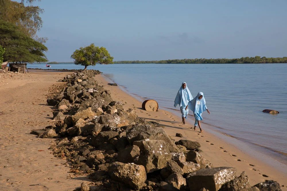 Girls walk along the shore of the beach on their way to school.