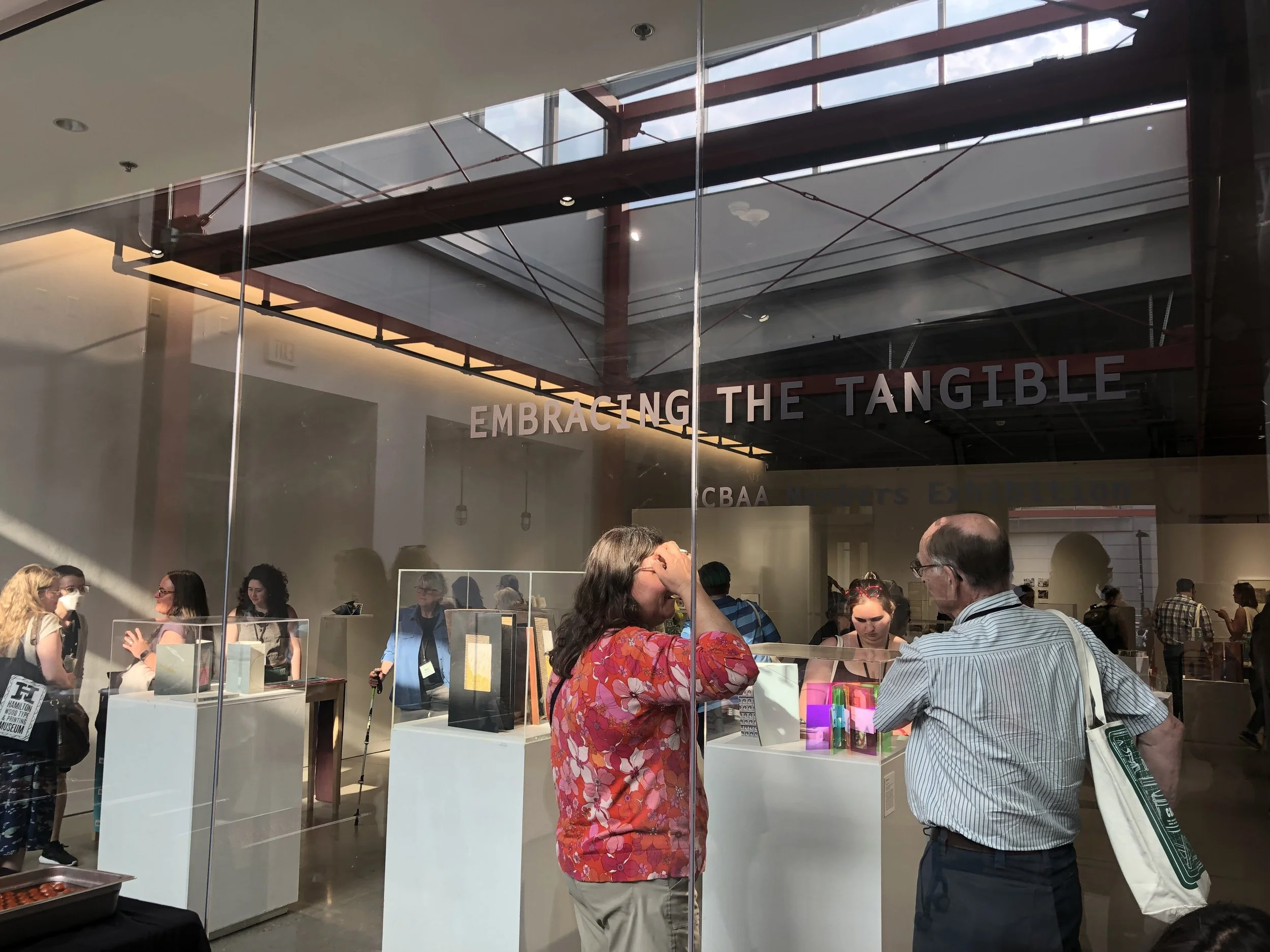 An art gallery full of people with "Embracing the Tangible" written on the glass entryway