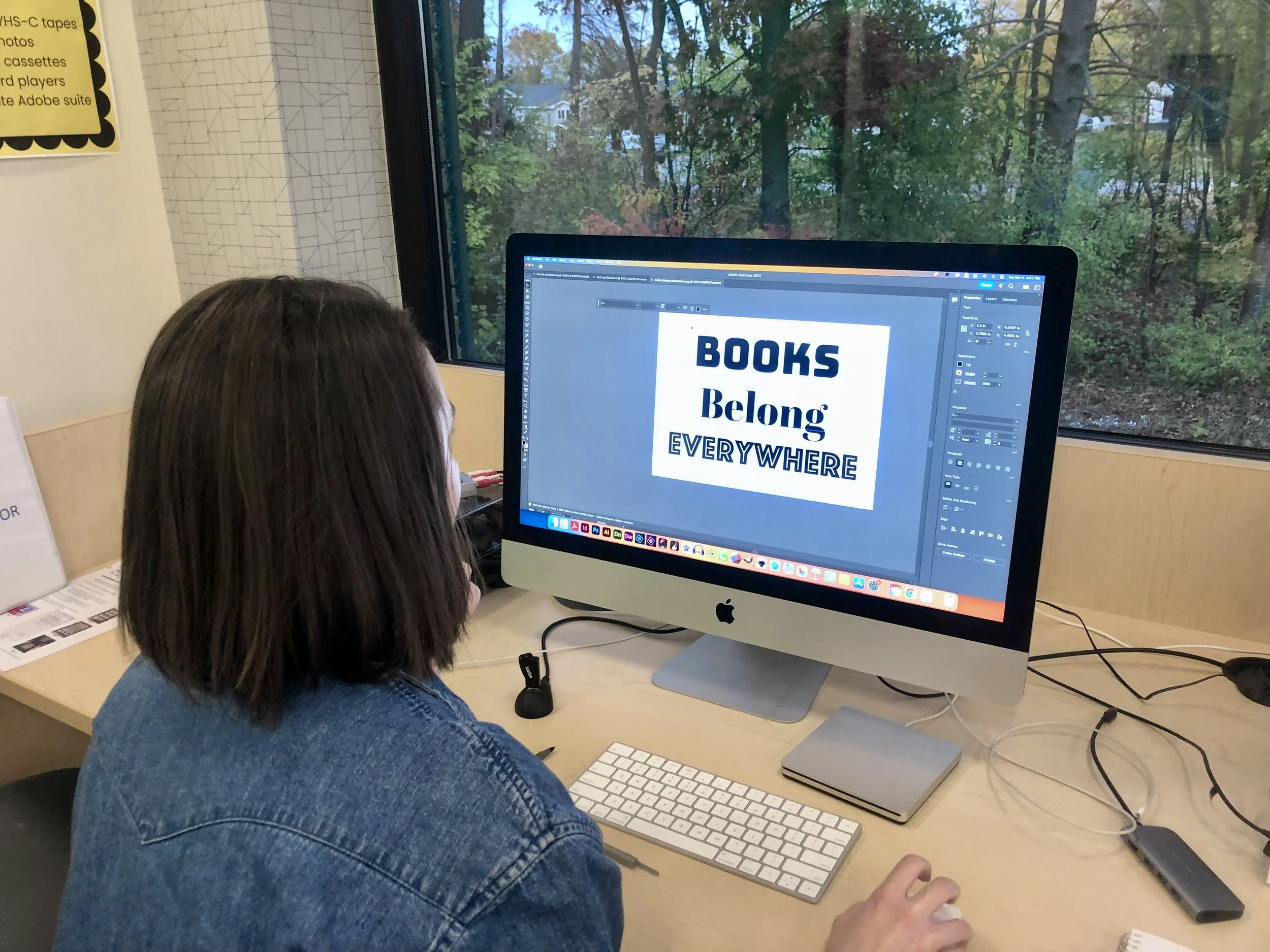 A woman sits at a computer with "Books Belong Everywhere" on the screen