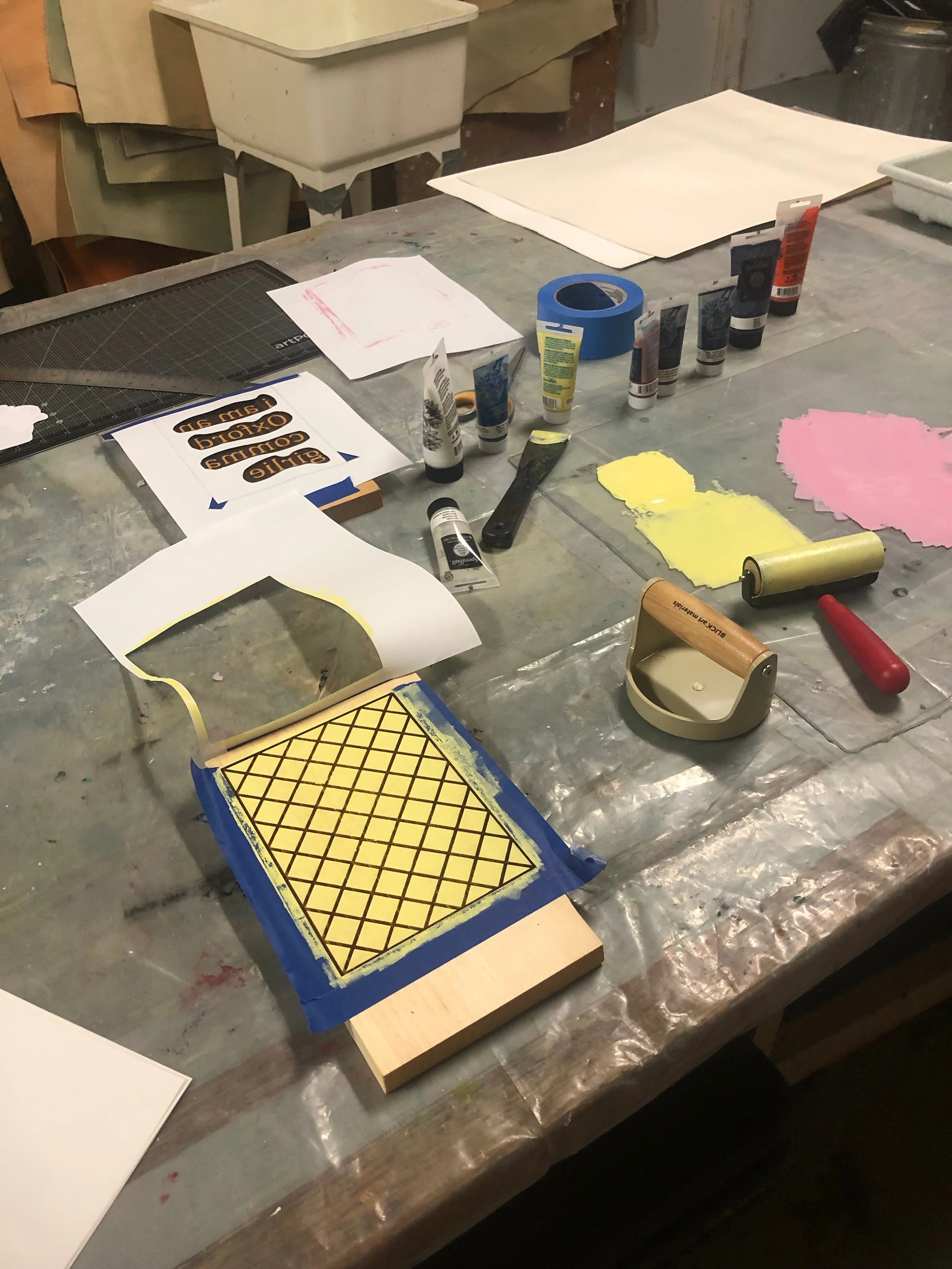 A table covered in ink, pressure tools, and an inked up plate with yellow ink.