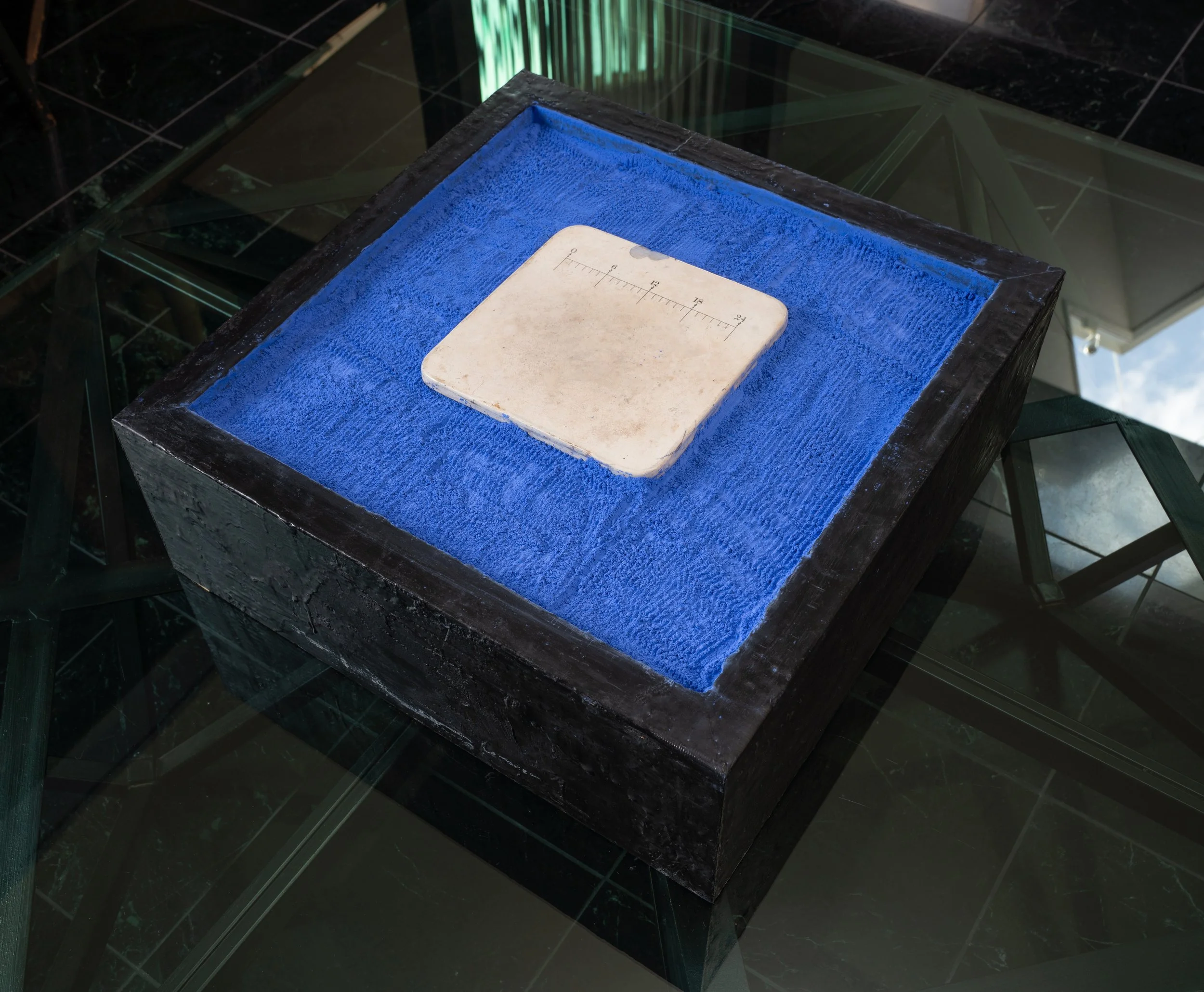 Black acrylic encaustic box frame 6" H. x 24" W. x 24” D. filled with blue carpenter chalk with white polished marbel square tablet centered.