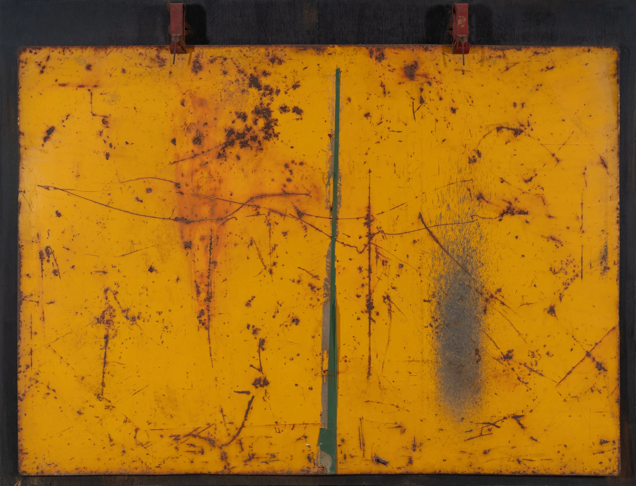 Horizontal presentation. Large yellow metal place with rusty marks, green line down center, hanging by two heavy metal clamps on a black painted board.