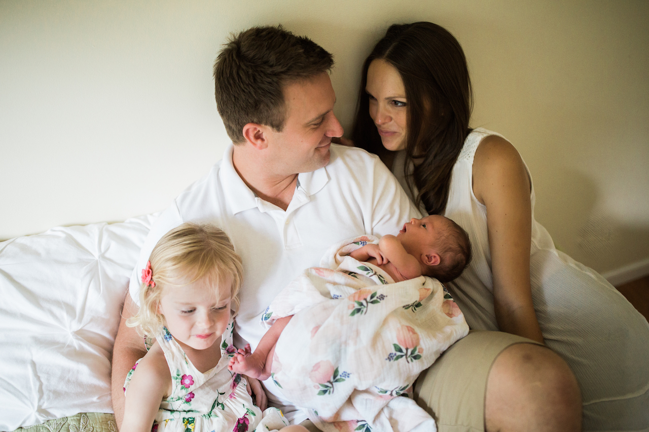 parents with two daughters on bed cuddling | cleveland, ohio newborn photography