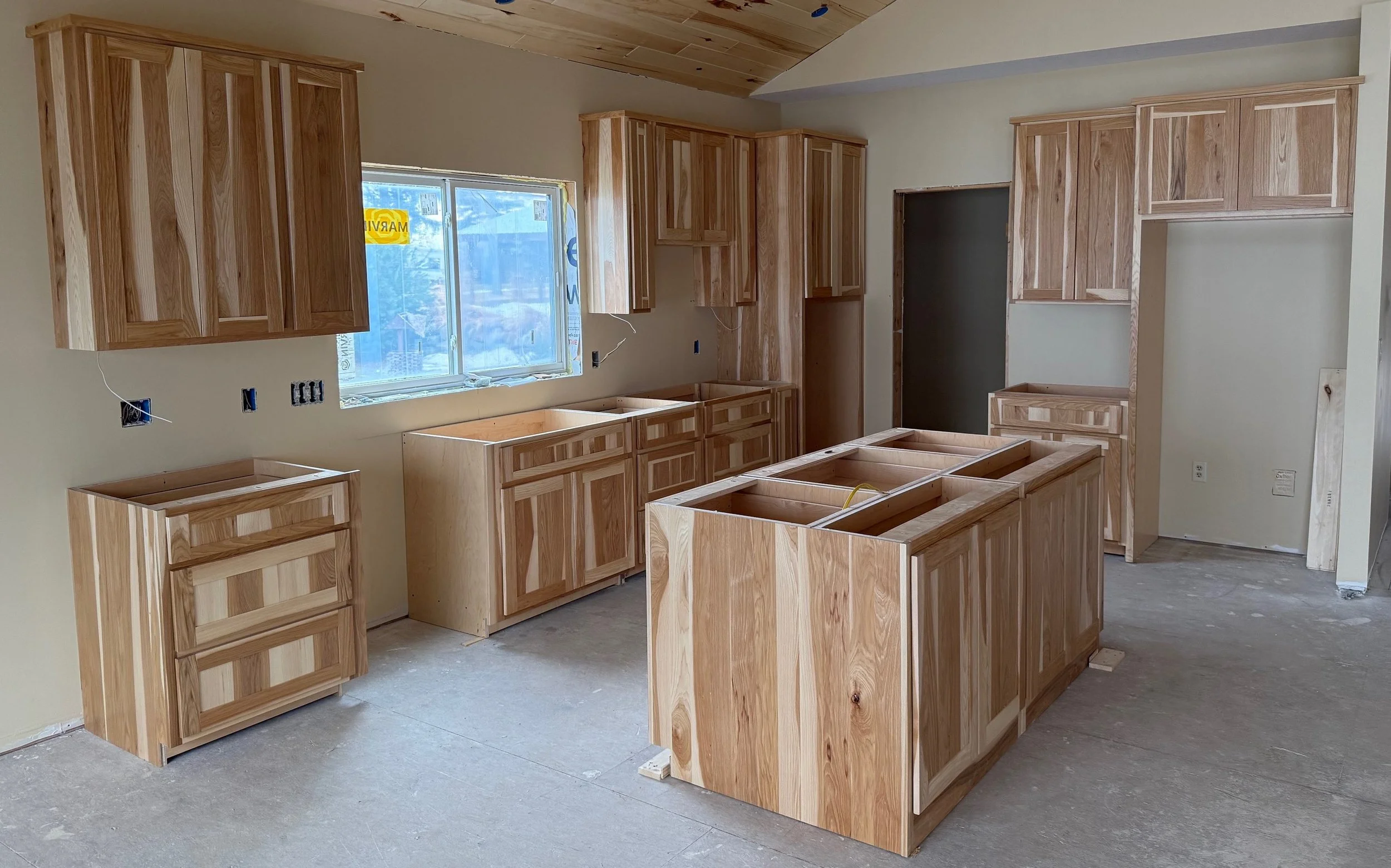 Kitchen under construction with unfinished wooden cabinets and drawers, a window, and a wooden ceiling.