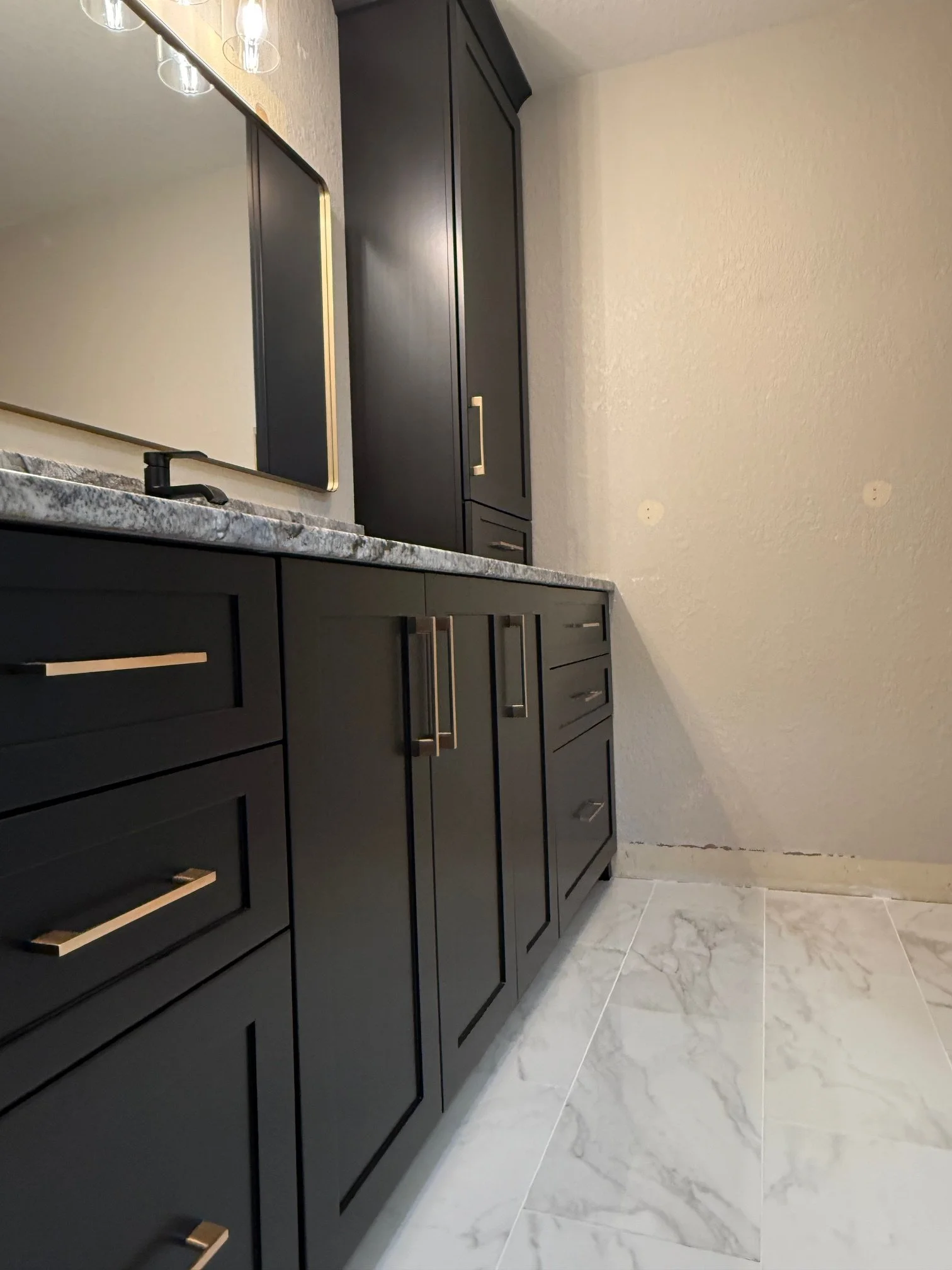 Interior bathroom with black cabinets, marble countertop, large mirror, black faucet, and tiled floor.