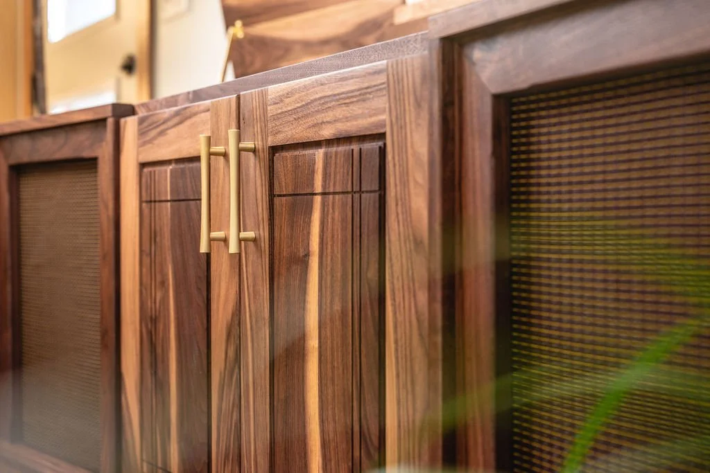 Close-up of a wooden cabinet with black mesh doors and gold handles.
