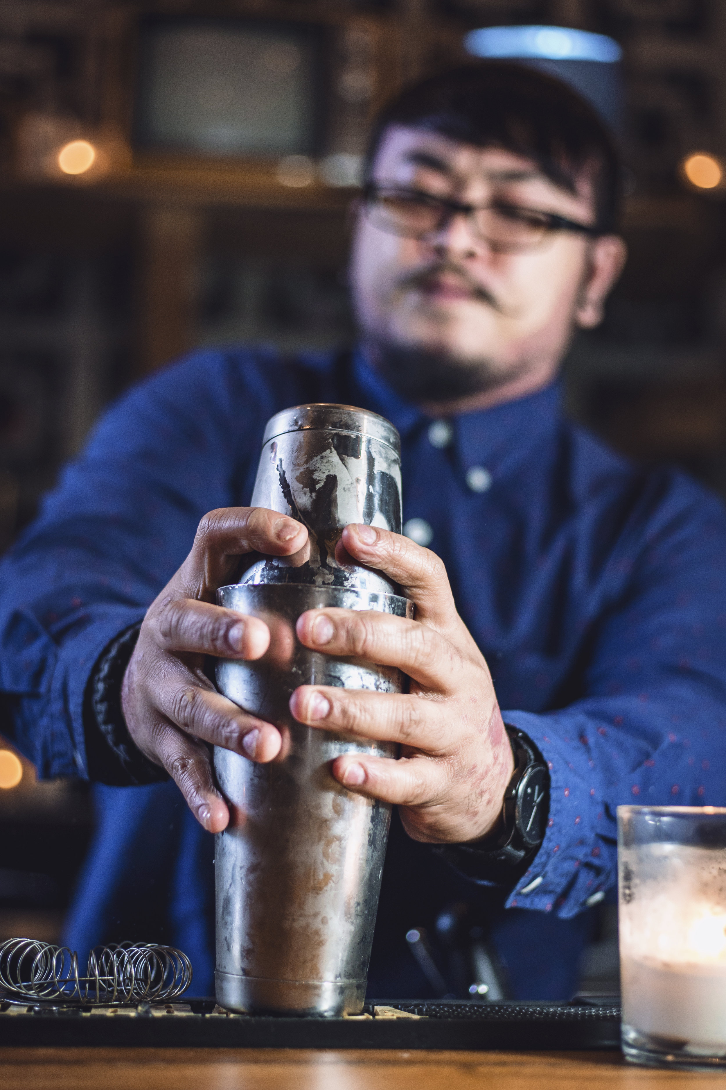 Asian man barista shaking iced black coffee in shaker and pouring in  cocktail glass on bar
