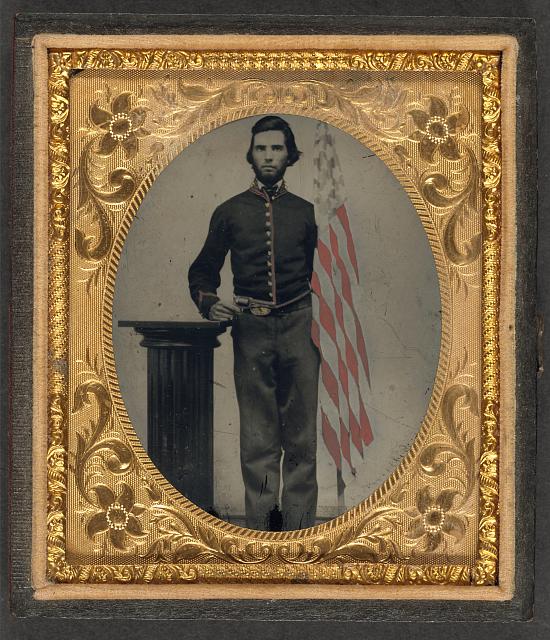 Soldier in Union Artillery Uniform Standing Next to Pedestal Holding Revolver and American Flag | Circa 1861-1865