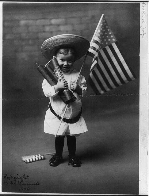 Little Boy Holding Three Large Firecrackers and an American Flag | Circa 1906