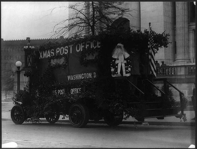 Santa Claus on the Back of a Washington D.C. Post Office Truck Decorated with Branches and an American Flag | Circa 1909