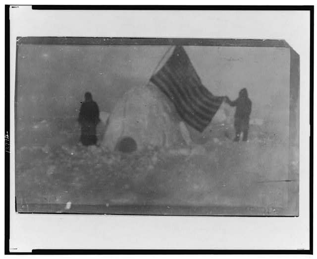 Two Members of Frederick Cook's Expedition with US Flag Stuck in Igloo at Expedition Camp Site at the North Pole | Circa 1909