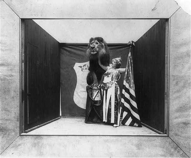 Woman with Stars and Eagle on Her Costume Holding a US Flag and Touching Tame Lion | Circa 1901