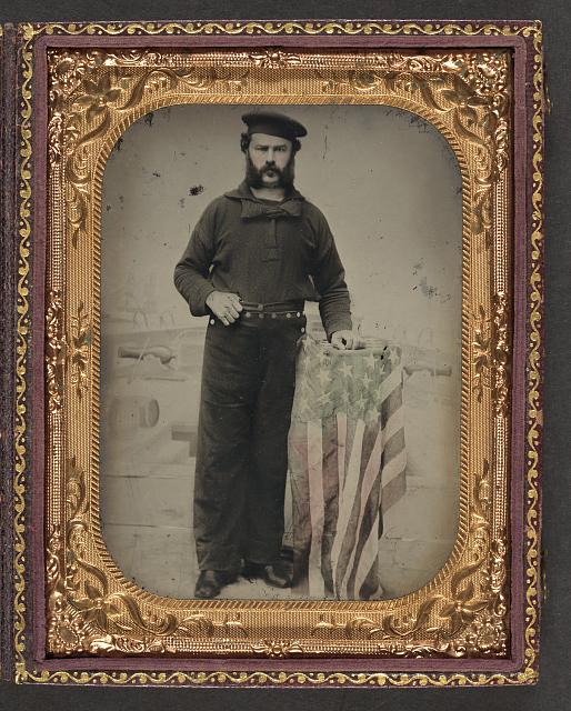 Sailor in Union Uniform at American Flag Draped Table in Front of Painted Backdrop Showing Naval Ship | Circa 1861-1865