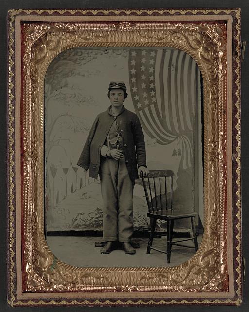 Soldier in Uniform with Arm in Sling in Front of Painted Backdrop Showing Military Camp and American Flag | Circa 1861-1865