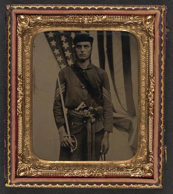 Soldier in Union Sergeant Uniform and Sash with Model 1840 Non-Commissioned Officer's Sword, Revolver, Cap Box, and Knife in Front of American Flag | Circa 1861-1865