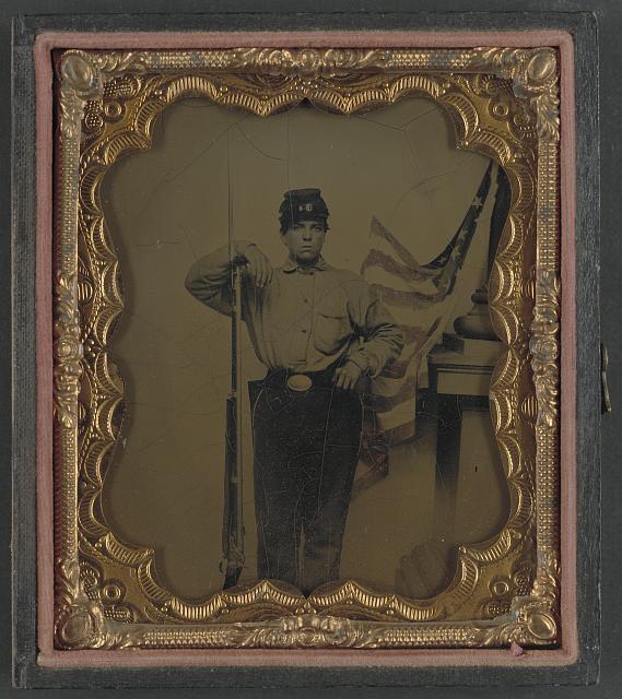 Soldier in Union Uniform with Bayoneted Musket in Front of Painted Backdrop Showing American Flag and Column Pedestal | Circa 1861-1865