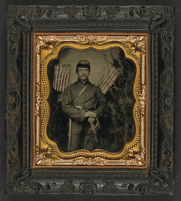 Soldier in Union Uniform with Shoulder Scales with Pearl-Handed Revolver and Saber in Front of Backdrop Showing Trees and Two Great Star Flags | Circa 1861-1865