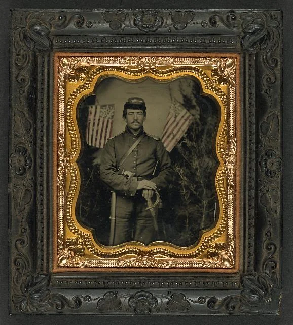 Soldier in Union Uniform with Shoulder Scales with Pearl-Handed Revolver and Saber in Front of Backdrop Showing Trees and Two Great Star Flags | Circa 1861-1865