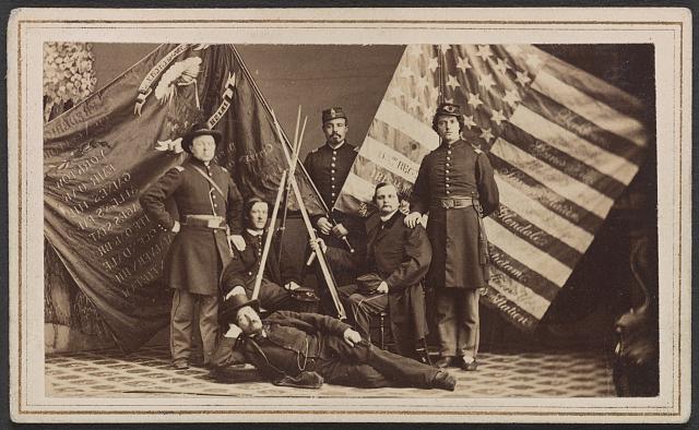Soldiers of 63rd New York Infantry Regiment in Uniform and One Man in Civilian Dress with Federal and State Battle Flags and Rifle Stack | Circa 1861-1865