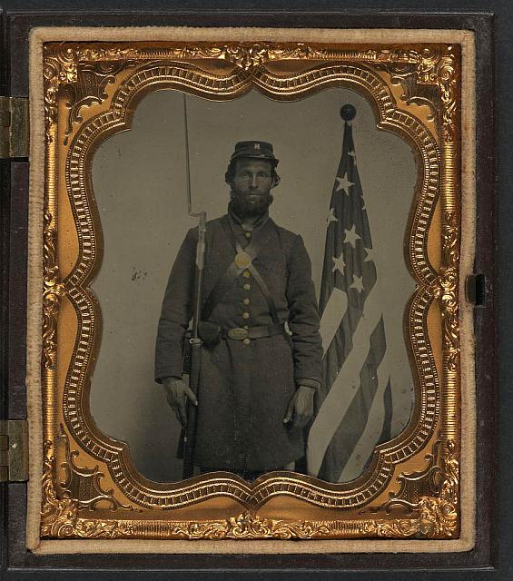 Soldier in Union Uniform and Company H Cap with Bayoneted Musket, Cap Box, and Volunteer Main Militia Belt Buckle in Front of American Flag | Circa 1861-1865