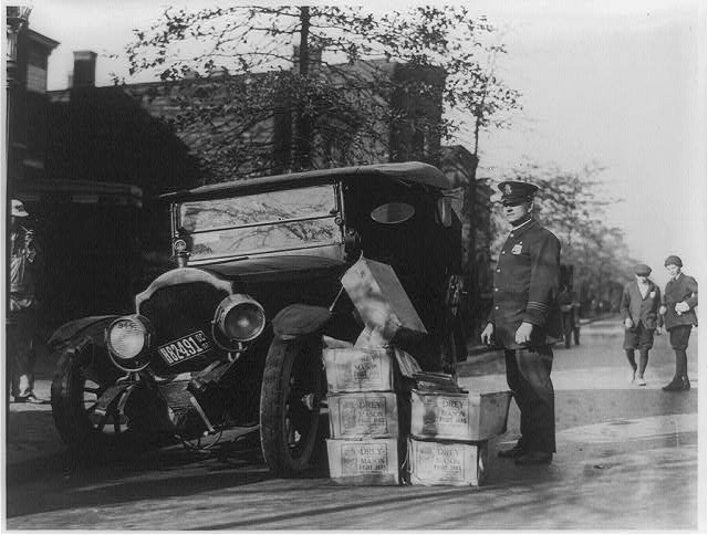 Policeman Standing Alongside Wrecked Car and Cases of Moonshine | Circa 1922