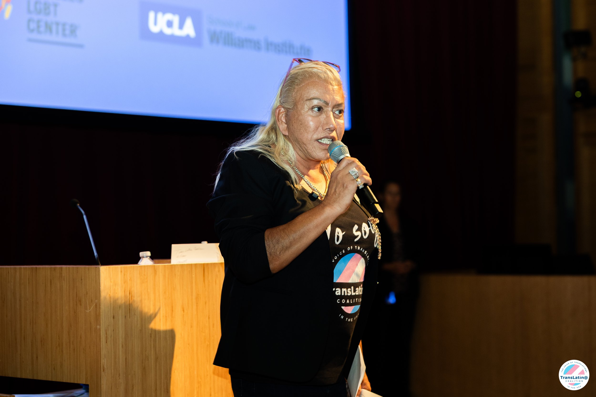Bamby Salcedo speaks into a handheld microphone at the front of the West Hollywood town hall.
