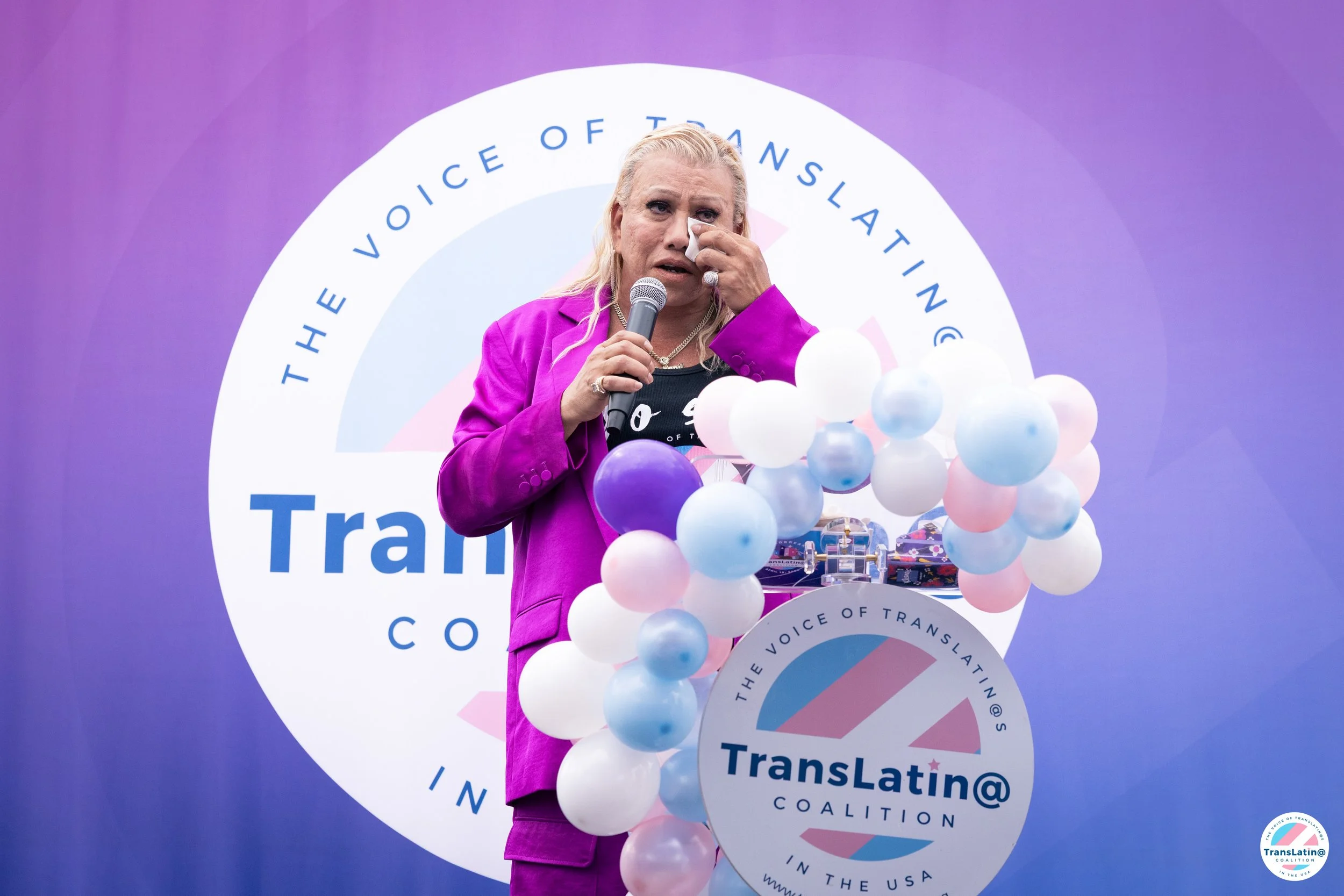 Bamby Salcedo speaks at a podium decorated with balloons and The TransLatin@ Coalition logo during the groundbreaking ceremony.