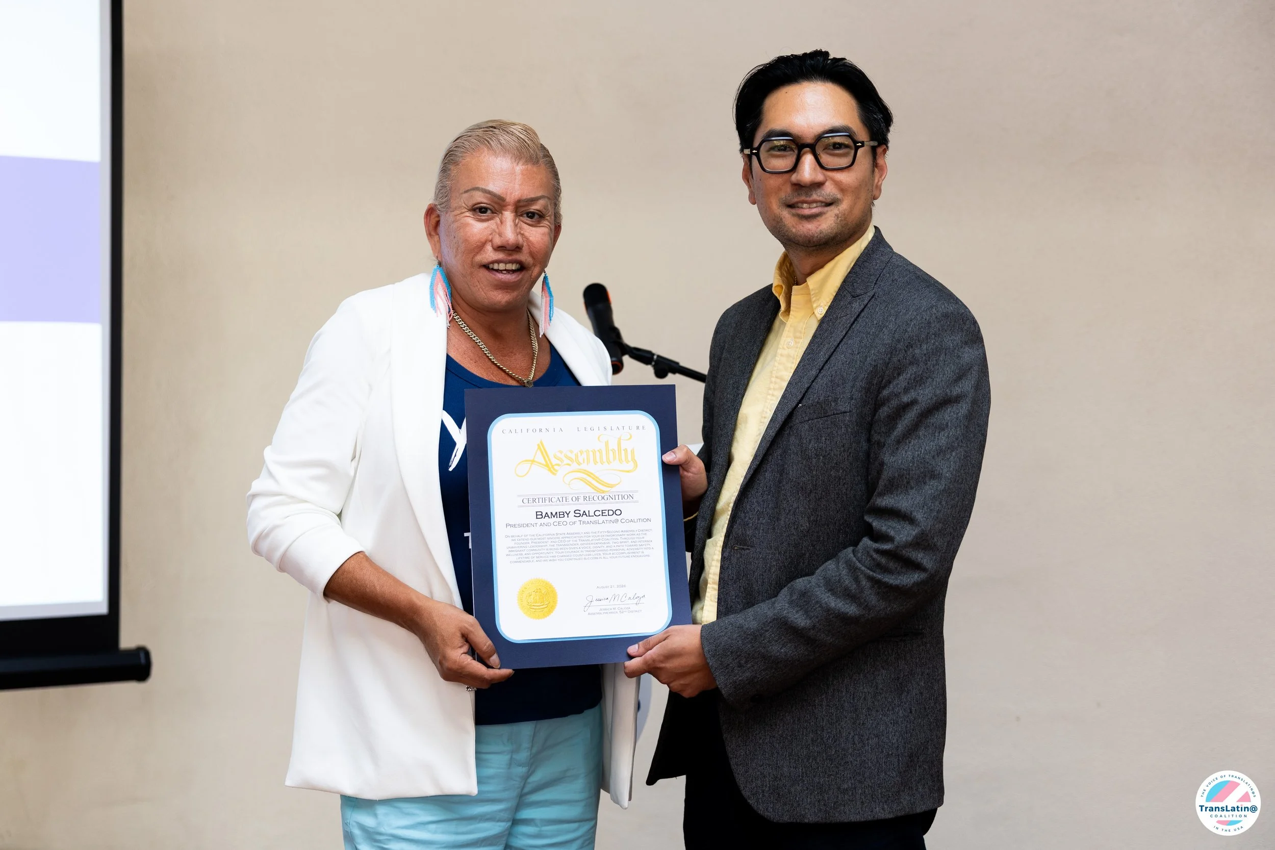 Bamby Salcedo receives a certificate recognizing her contributions to the Trans Pláticas research report.