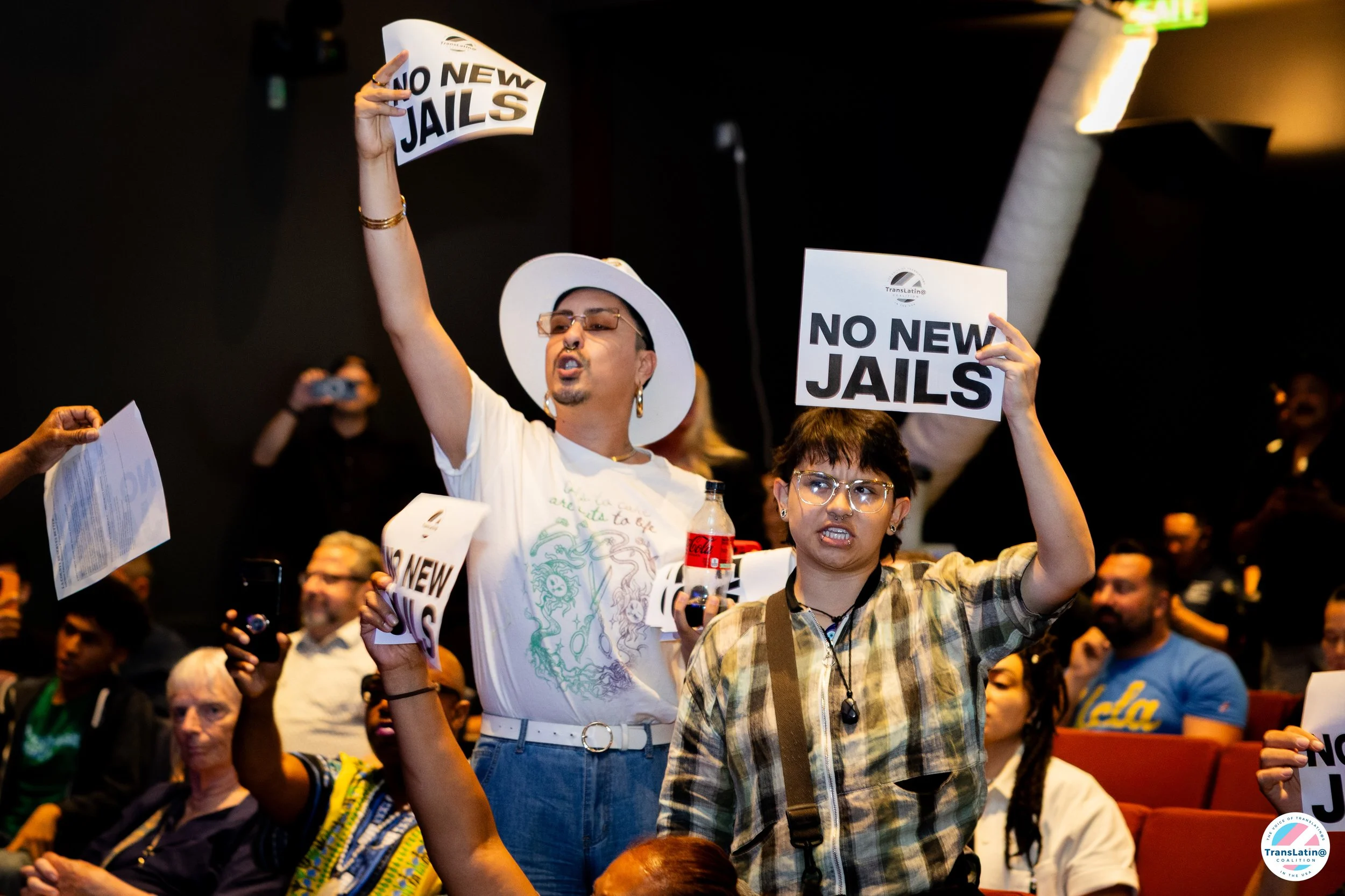 Two community members hold “No New Jails” signs above their heads during the town hall action.