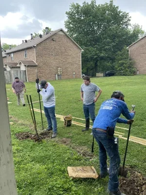 K&C Fence team members set fence posts along a grassy property line during an installation in Tennessee, with tools and materials laid out across the yard.